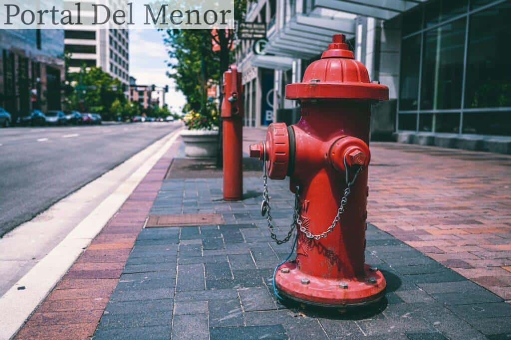 Red fire hydrant with chains located on empty street near road and building on sunny day