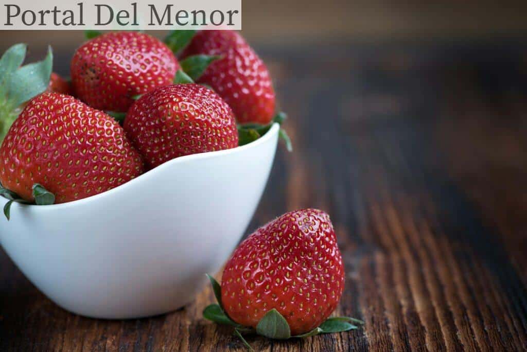Close-up of fresh strawberries in a white bowl on a rustic wooden table, highlighting vibrant red color.